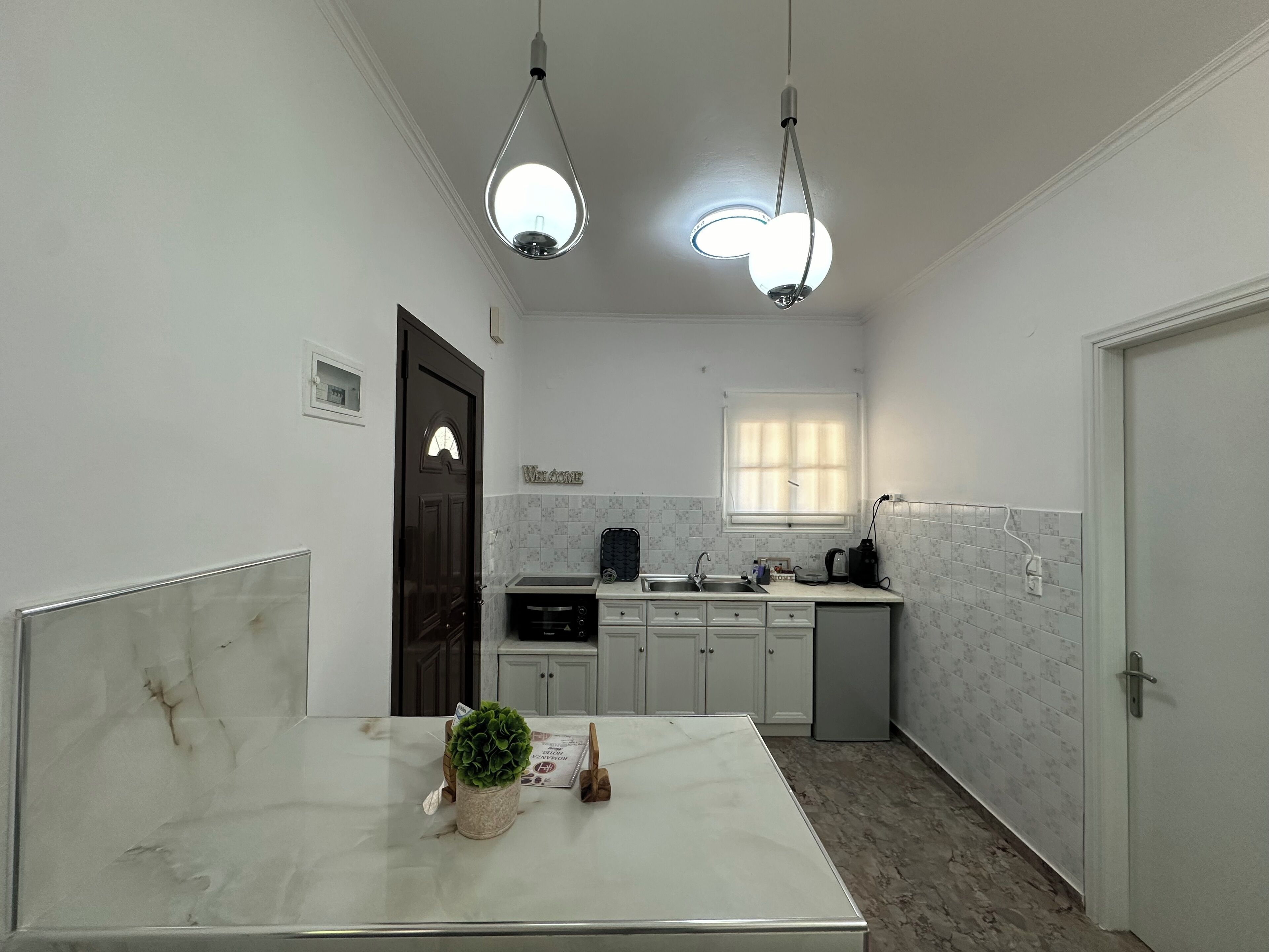 A modern kitchen with white cabinets, a marble countertop, and a window with blinds.