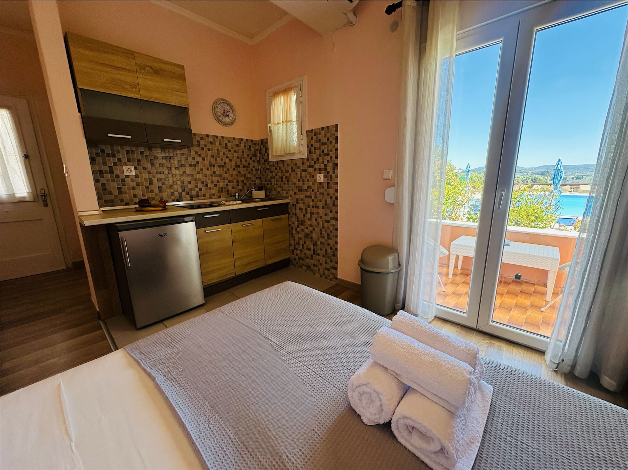 A hotel room with a bed, a small kitchenette, a view of the outdoors, and a sliding glass door.
