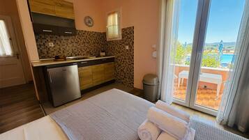 A hotel room with a bed, a small kitchenette, a view of the outdoors, and a sliding glass door.