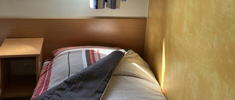A bedroom with a bed, a window with curtains, a small bedside table, and a view of greenery outside.