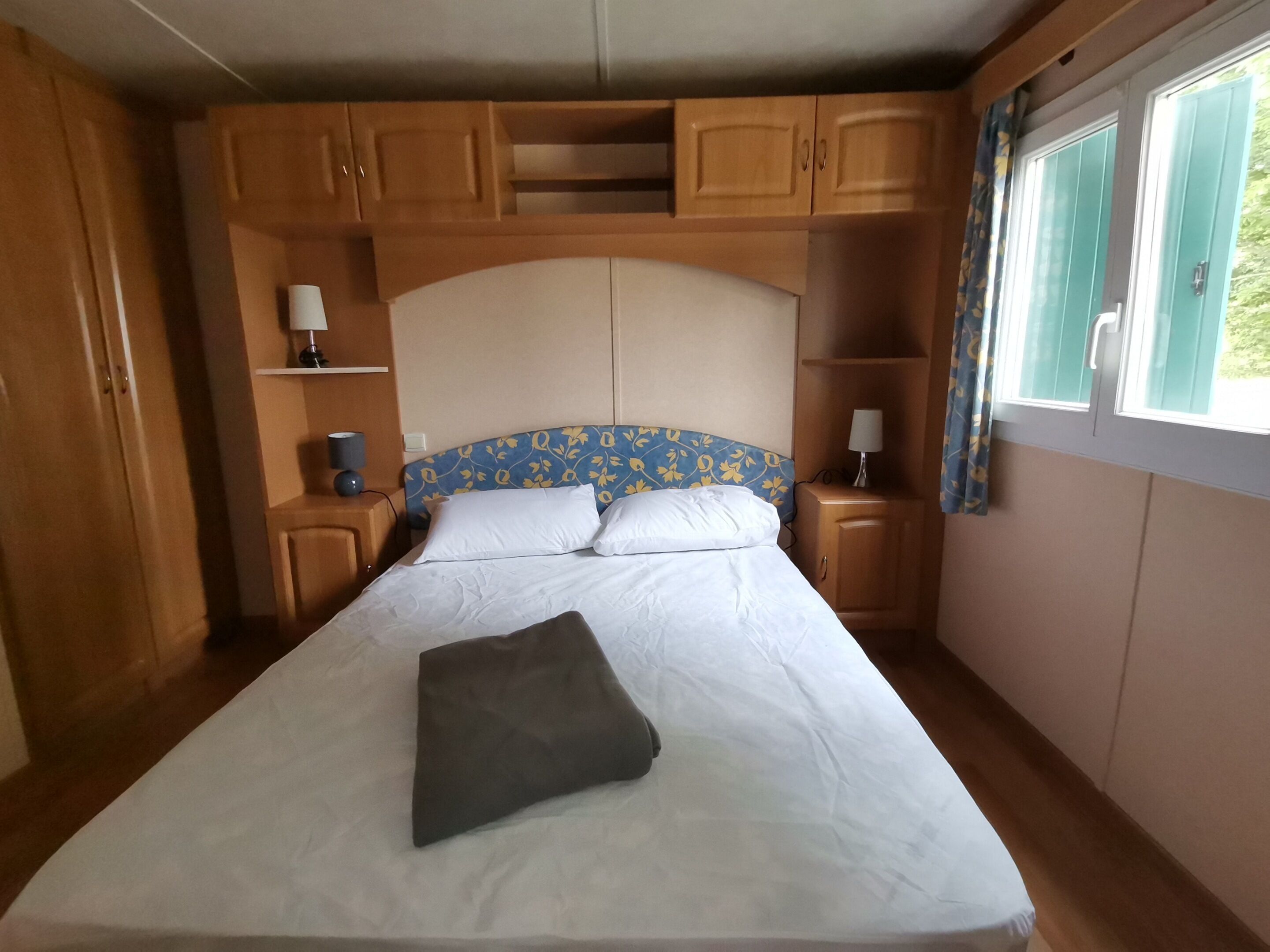 Une chambre à coucher avec un lit, des armoires en bois et une fenêtre avec des rideaux.