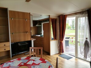 Une chambre compacte dotée d’une kitchenette, d’une télévision, d’un bureau en bois et offrant une vue sur l’extérieur.