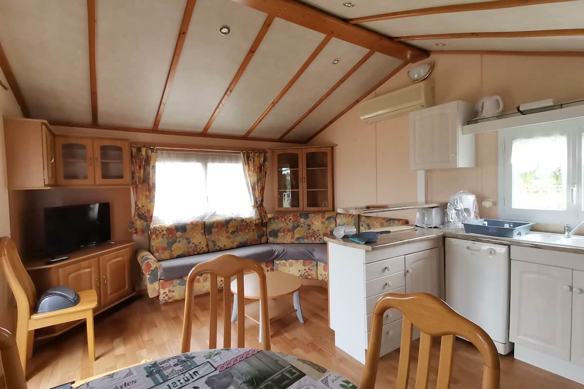 Una cocina compacta con comedor, televisor y ventana con cortinas.