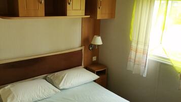Ein Schlafzimmer mit einem Bett, weißen Kissen, einem Nachttisch, einer Wandleuchte und Holzschränken über dem Bett.
