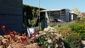 Un edificio moderno con cerramiento de vidrio, un jardín con diversas plantas y mesas al aire libre.