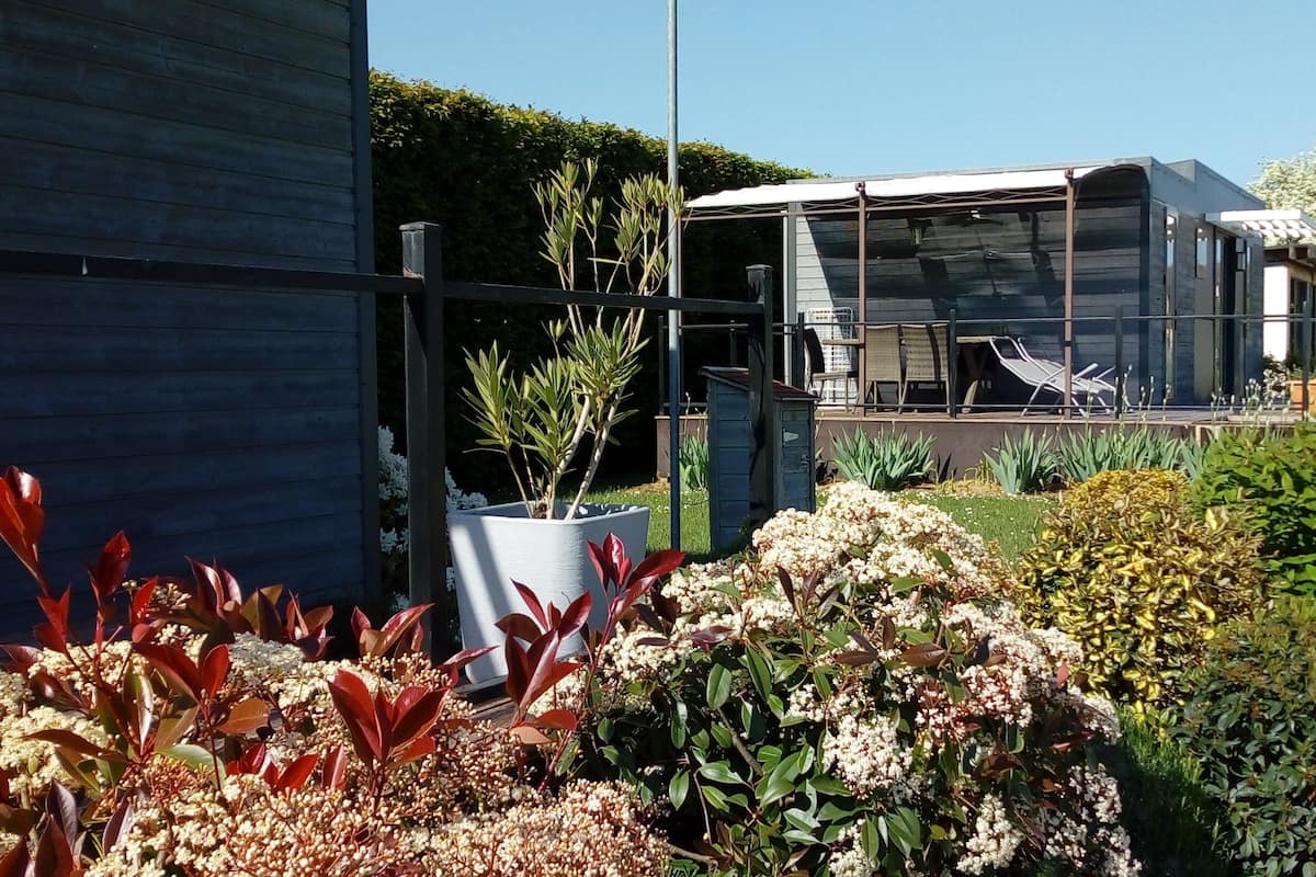 Un edificio moderno con cerramiento de vidrio, un jardín con diversas plantas y mesas al aire libre.