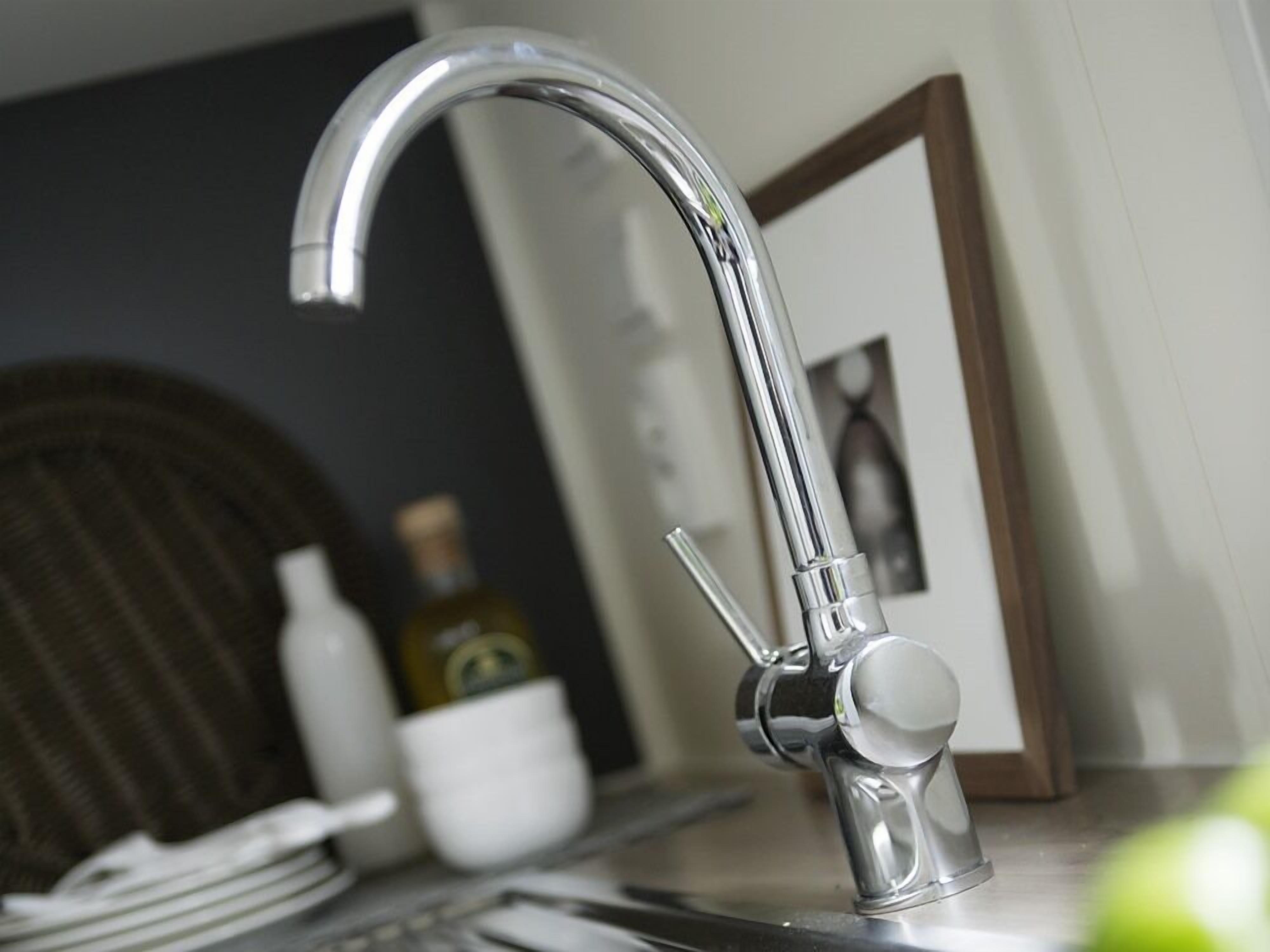 A modern kitchen with a stainless steel faucet, a wicker chair, a white mug, and a bottle of olive oil on the counter.