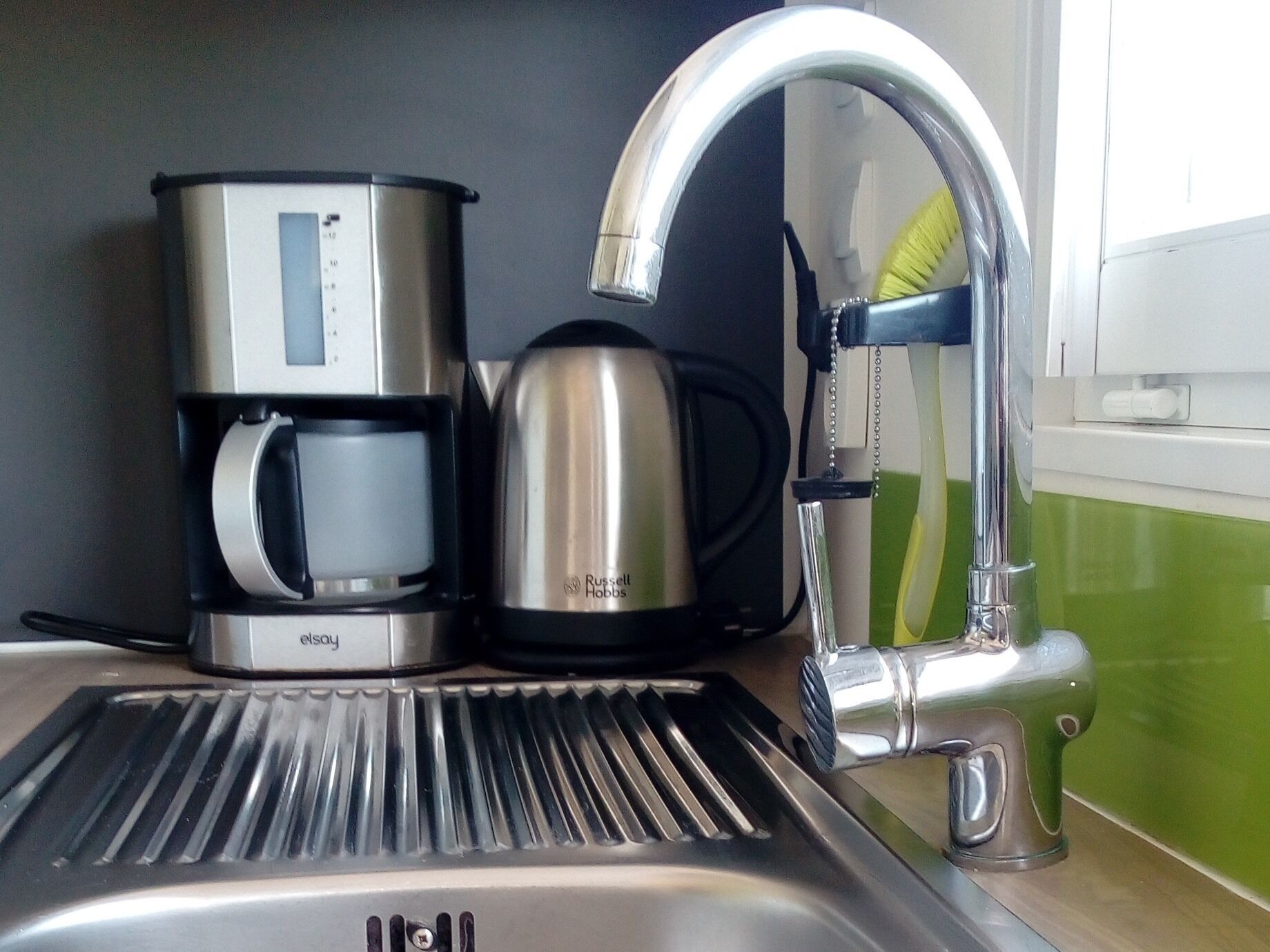 A kitchen sink with a modern faucet, a coffee maker, and a kettle.