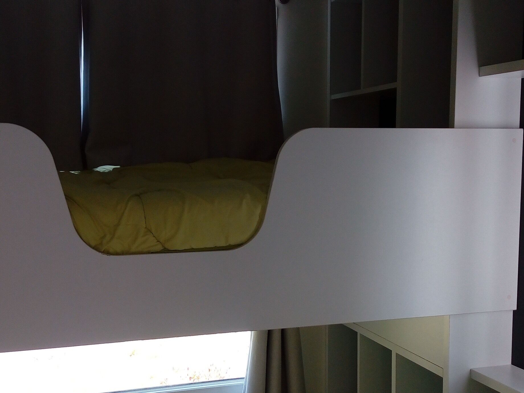 Een stapelbed met een gele matras en een raam met gordijnen.