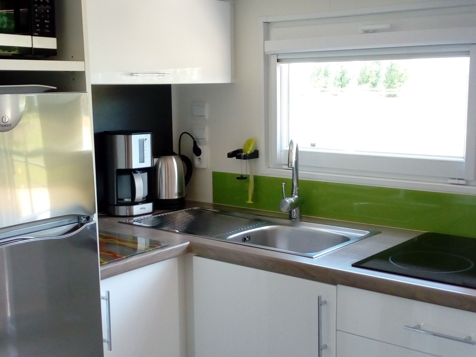 Una cucina moderna con un frigorifero in acciaio inox, una macchina da caffè e un lavello con una finestra sopra.