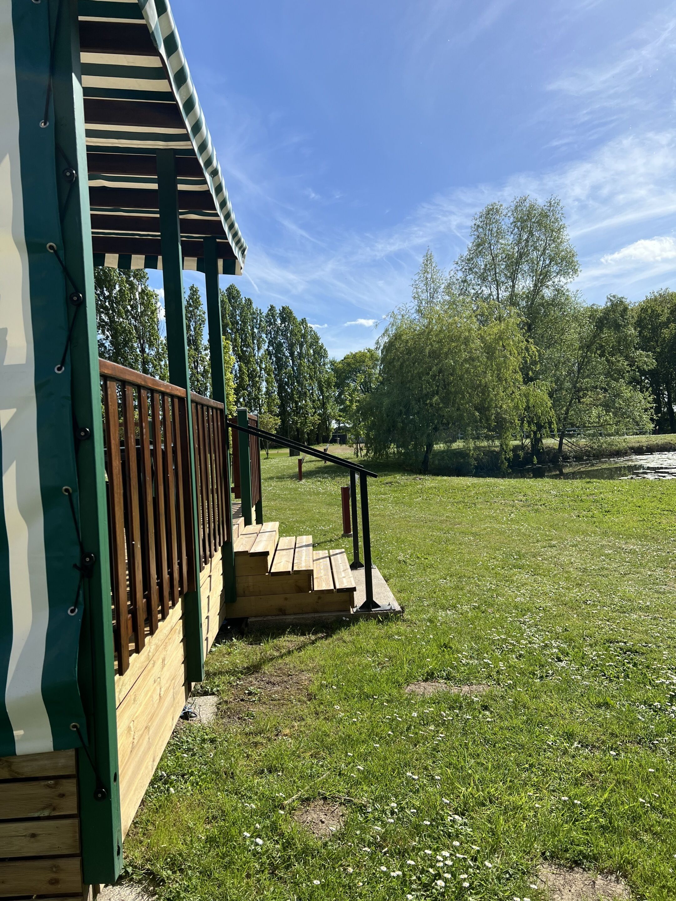 A wooden deck with a railing, a grassy area, and trees in the background.