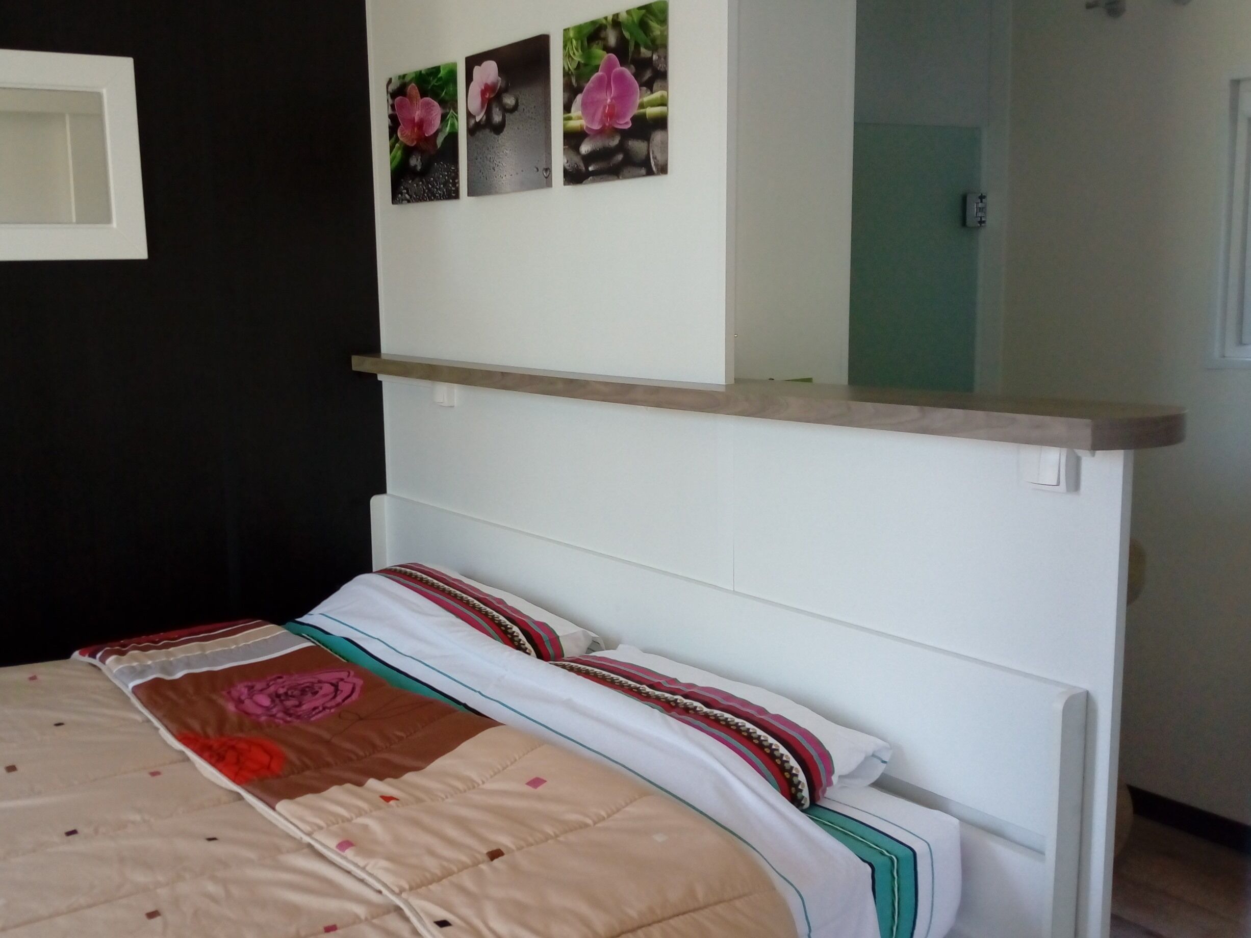 A bedroom with a bed, a bedside table, and a wall-mounted shelf with three flower photographs.