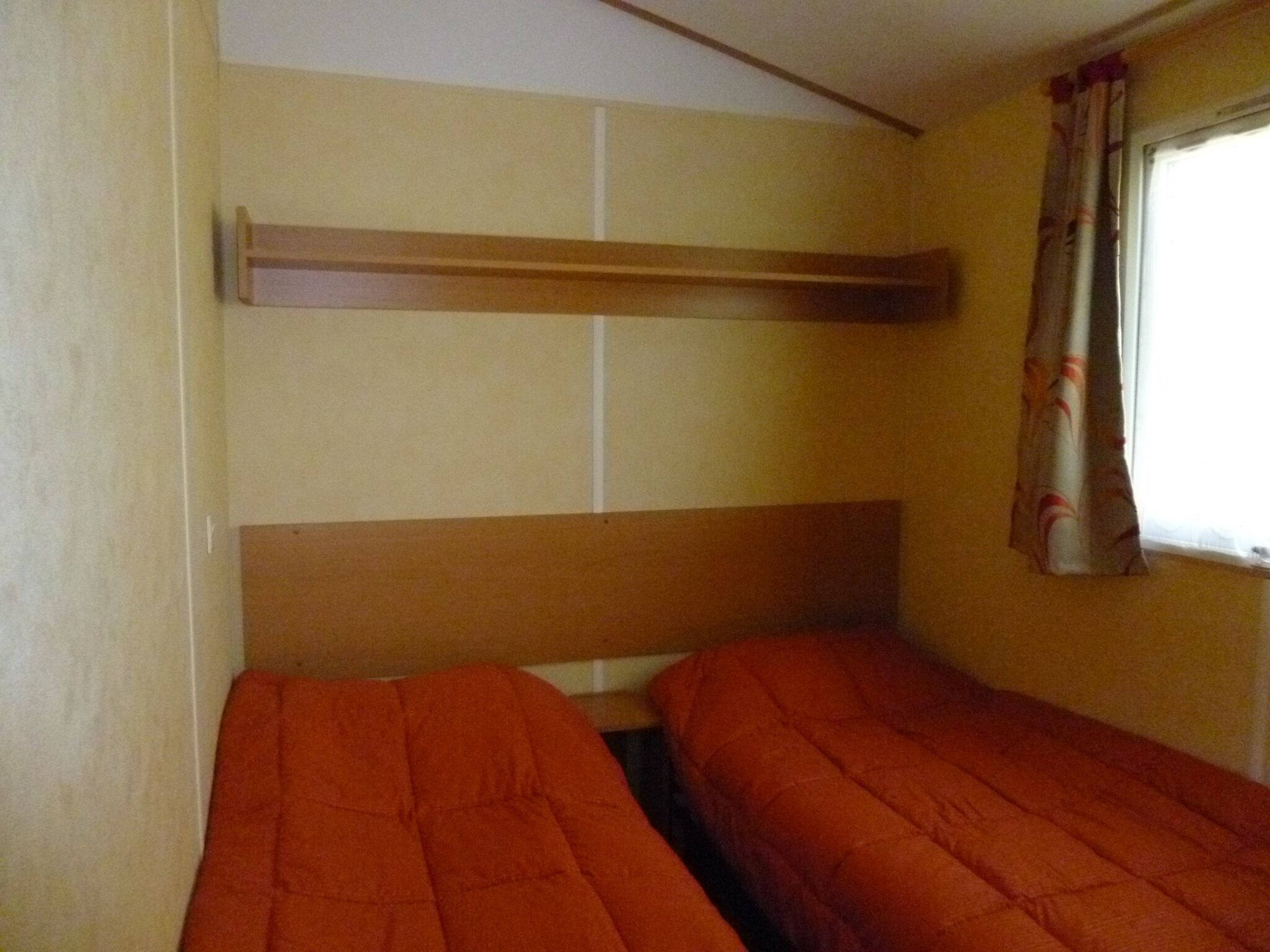 Una cama individual con cabecera de madera y una ventana con cortinas.