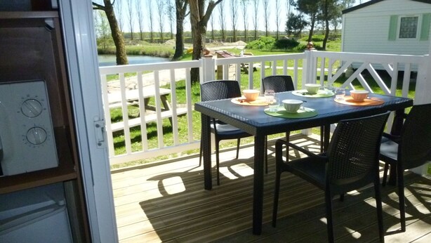 Una terraza con una mesa dispuesta para cuatro, con vistas a un área verde y un pequeño edificio blanco.