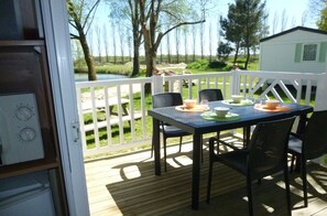 Una terraza con una mesa dispuesta para cuatro, con vistas a un área verde y un pequeño edificio blanco.