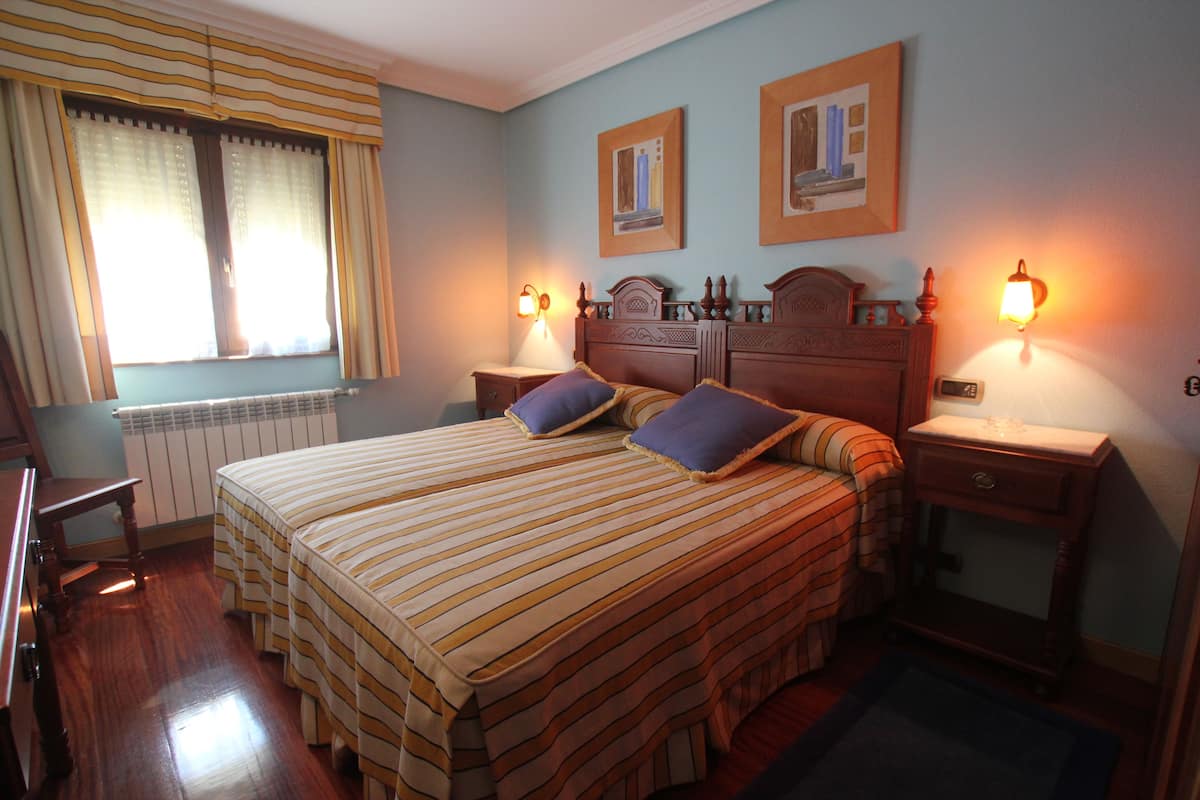 A hotel room with a large bed, two bedside tables with lamps, a chair, and a window with curtains.