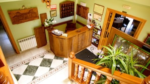 A reception area with a check-in counter, wooden cabinets, a radiator, a patterned floor, and a staircase. - Posada El Iso (Santillana del Mar)