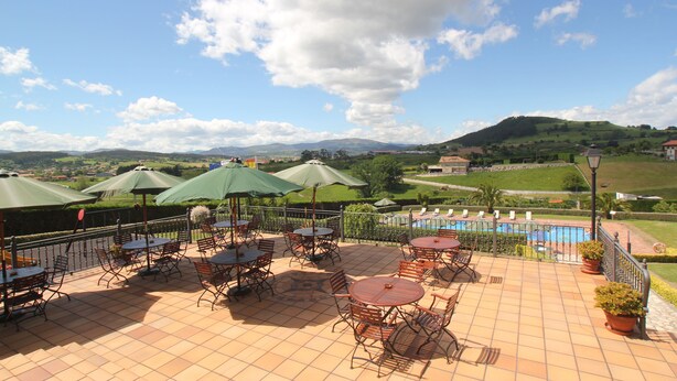 A terrace with outdoor seating and a view of a pool and hills. - Posada El Iso (Santillana del Mar)
