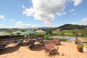 Una terraza con mobiliario exterior y vistas a una piscina y colinas.
