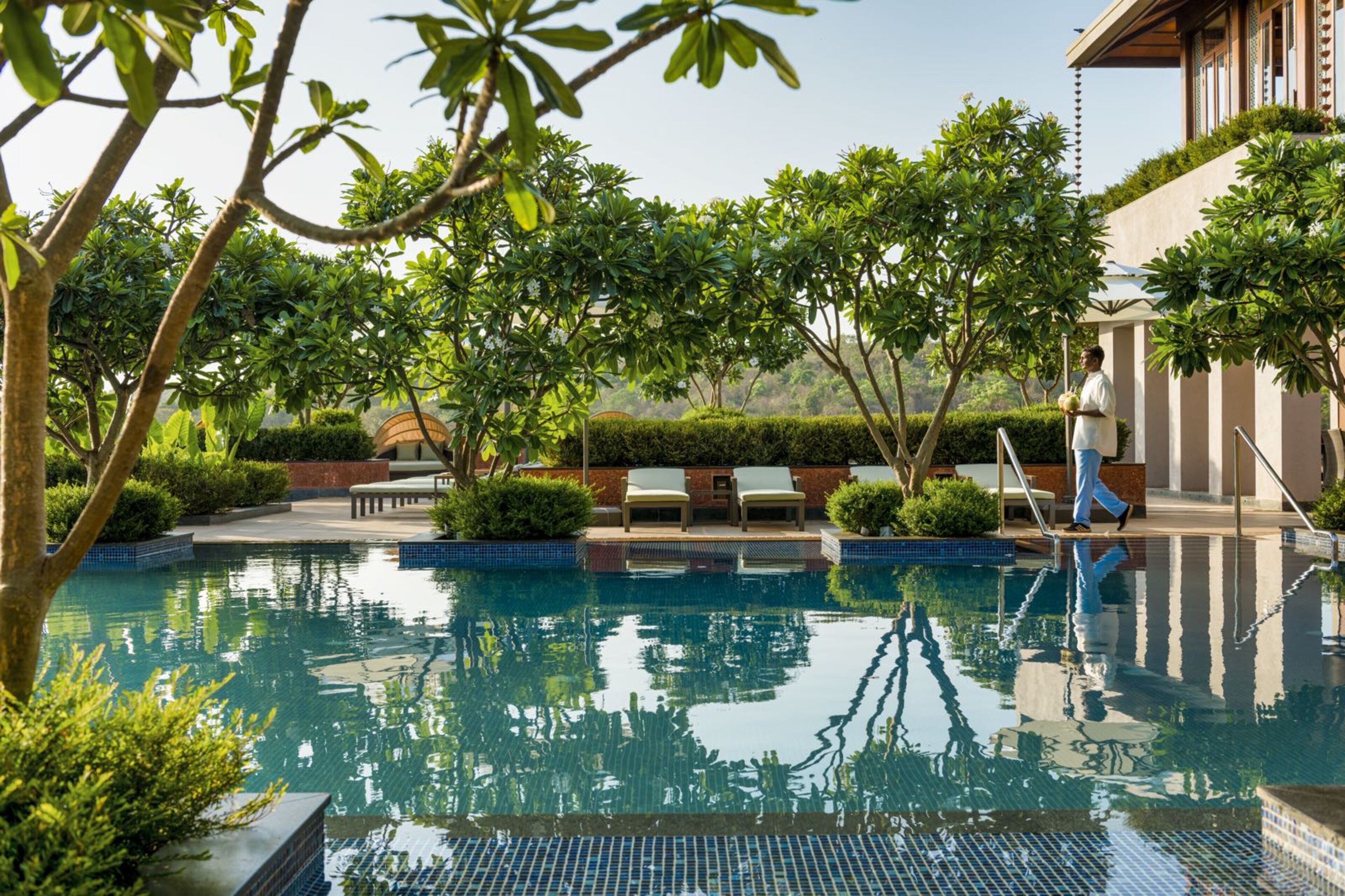 A pool area with lounge chairs, a person walking, and a building with a balcony.