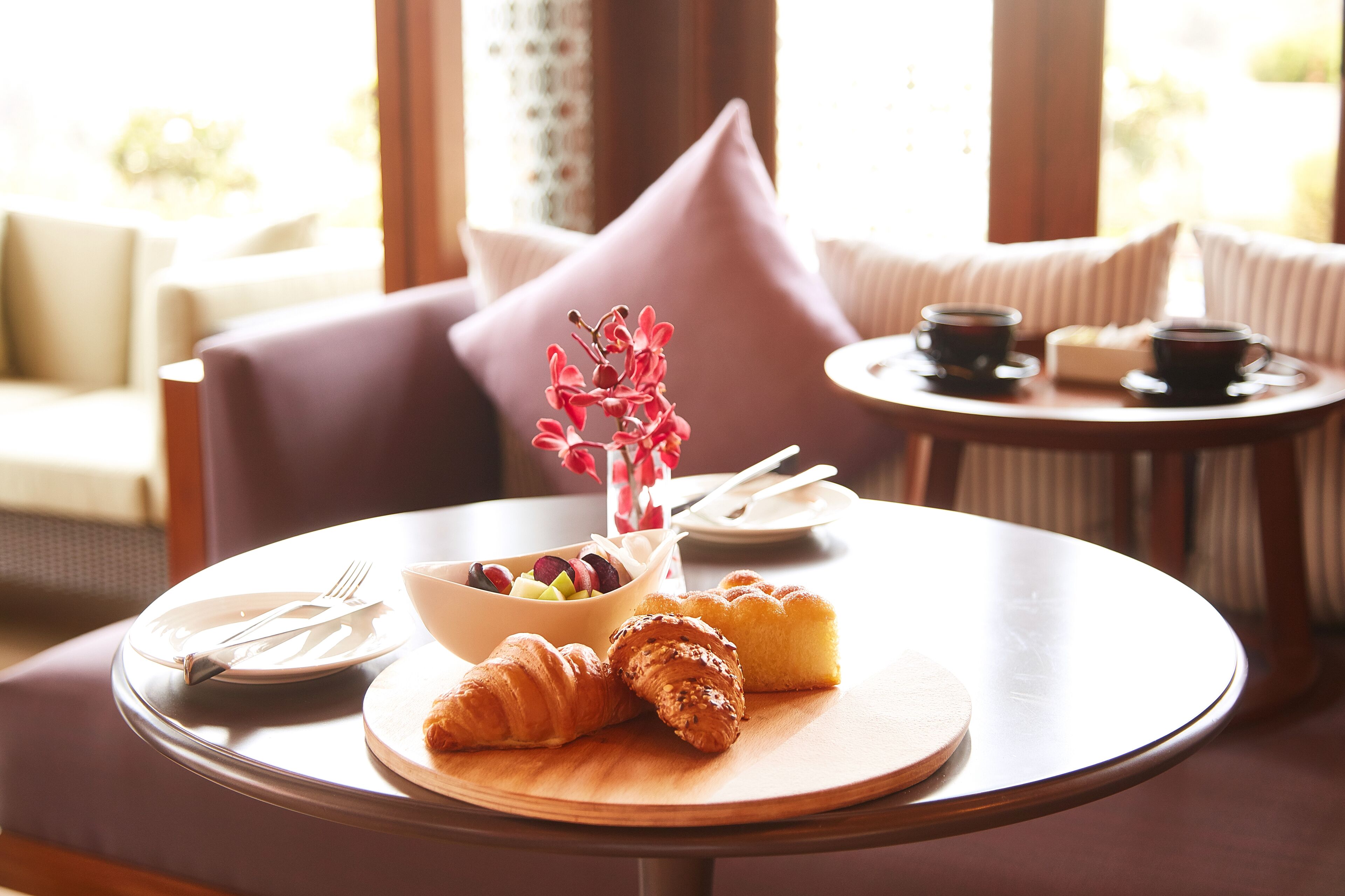 A round wooden table with croissants, a bowl of fruit, and a vase of flowers.