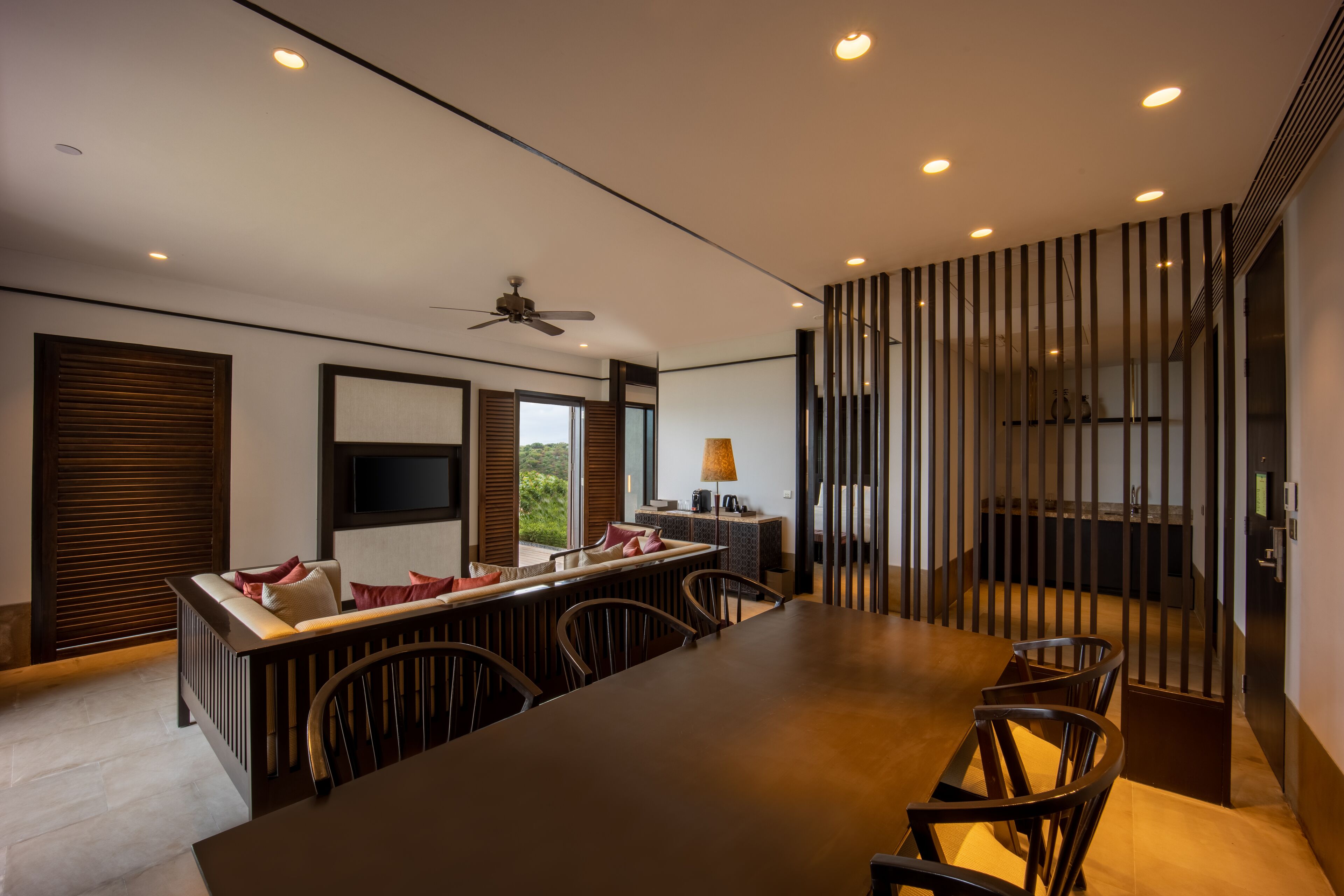 A modern dining area with a long table, chairs, a ceiling fan, and a TV mounted on the wall.