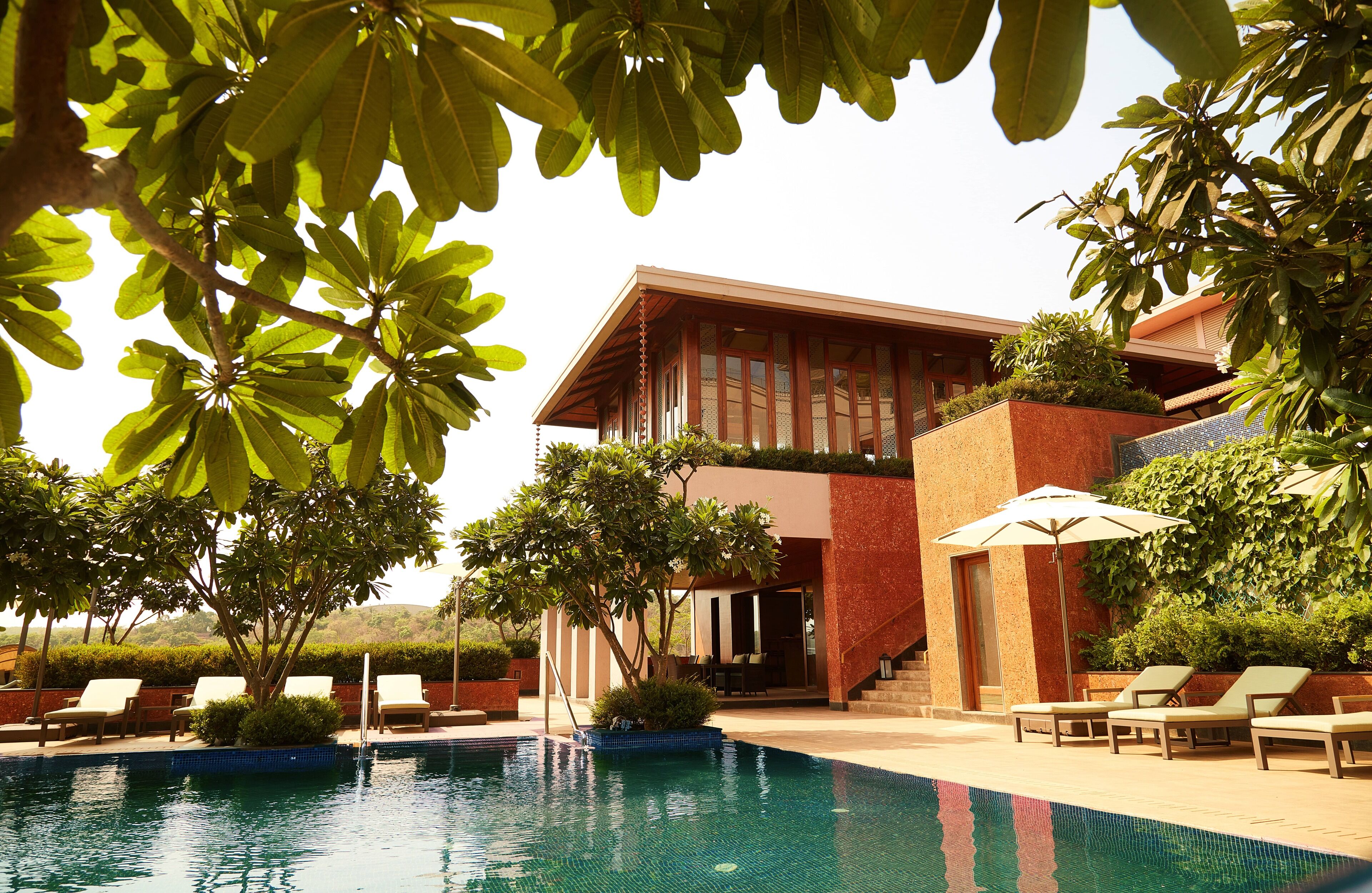 A modern building with a pool, surrounded by greenery and sun loungers.