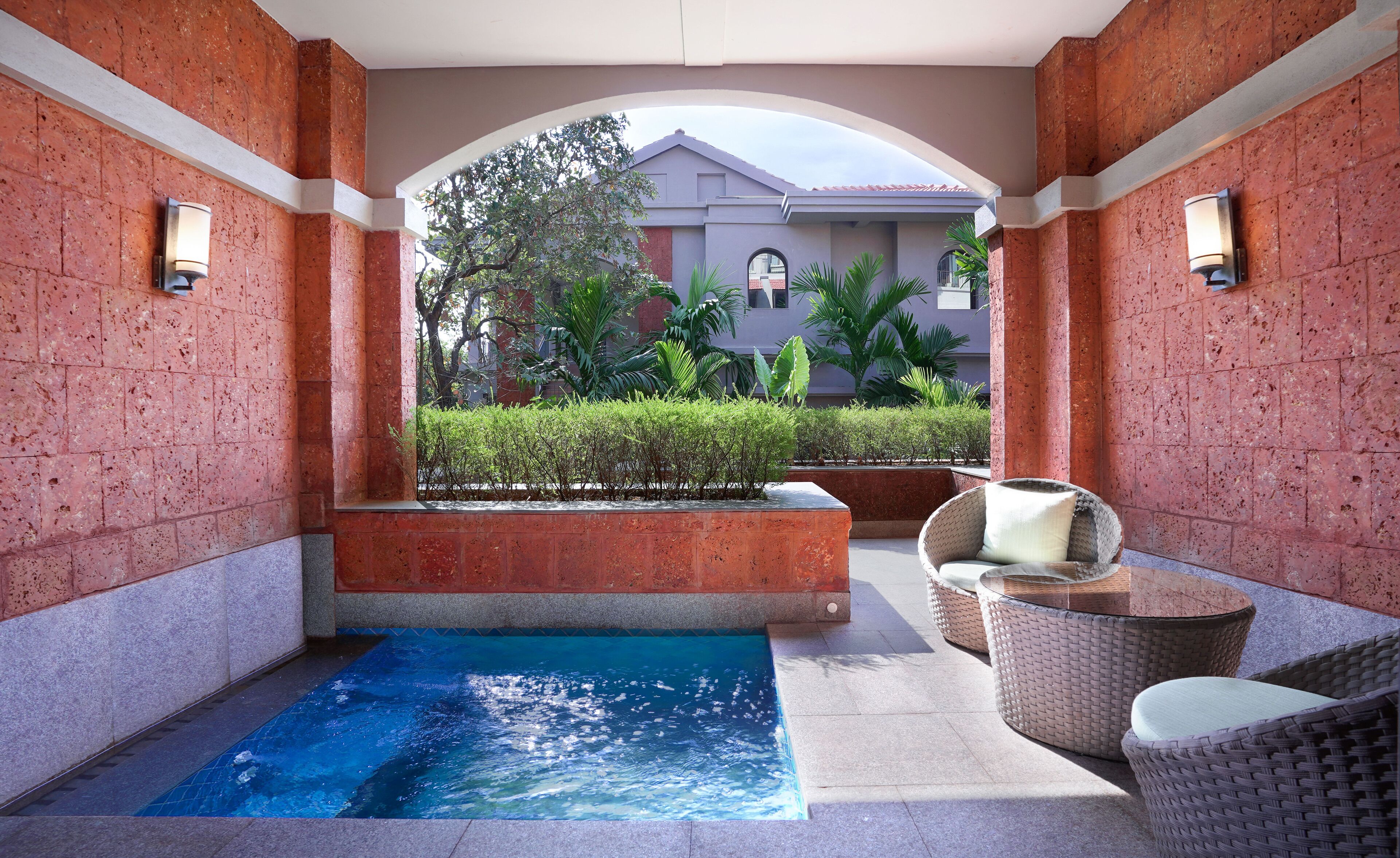 A spa area with a small pool, wicker chairs, and a view of a building in the background.