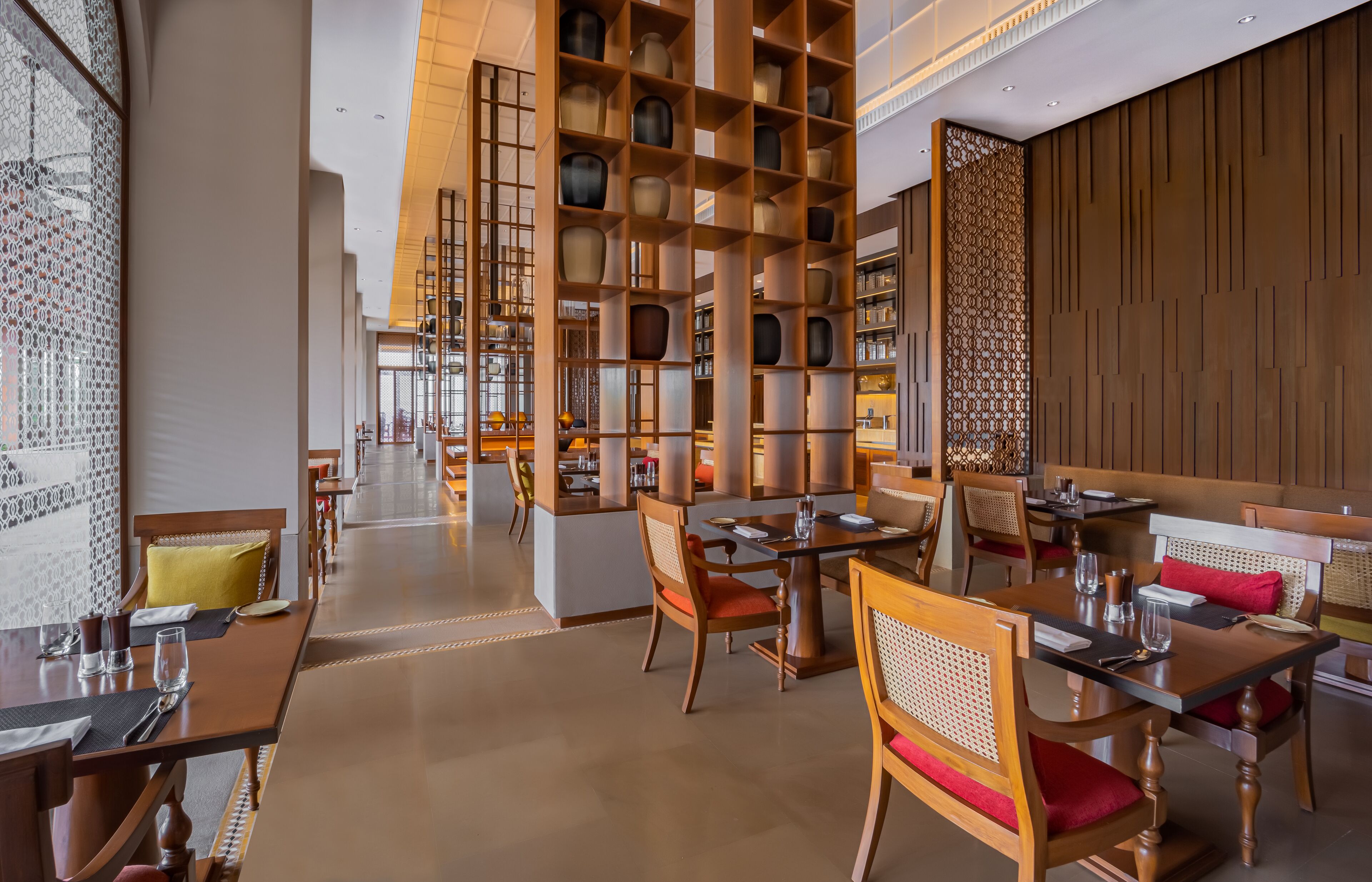 A restaurant with wooden tables and chairs, a central serving area, and a decorative wall with shelves.