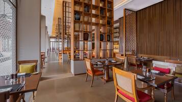 A restaurant with wooden tables and chairs, a central serving area, and a decorative wall with shelves.