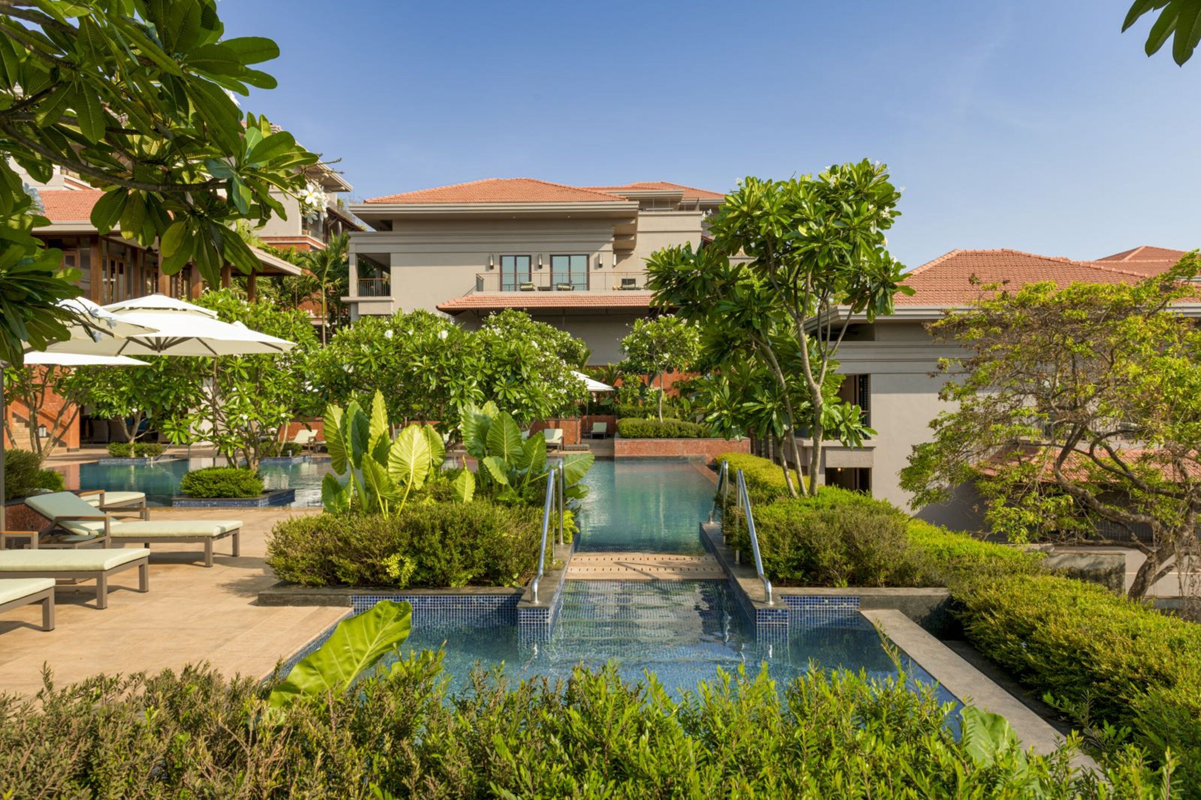 A pool area with lounge chairs, a small pool, and a building with a red-tiled roof.