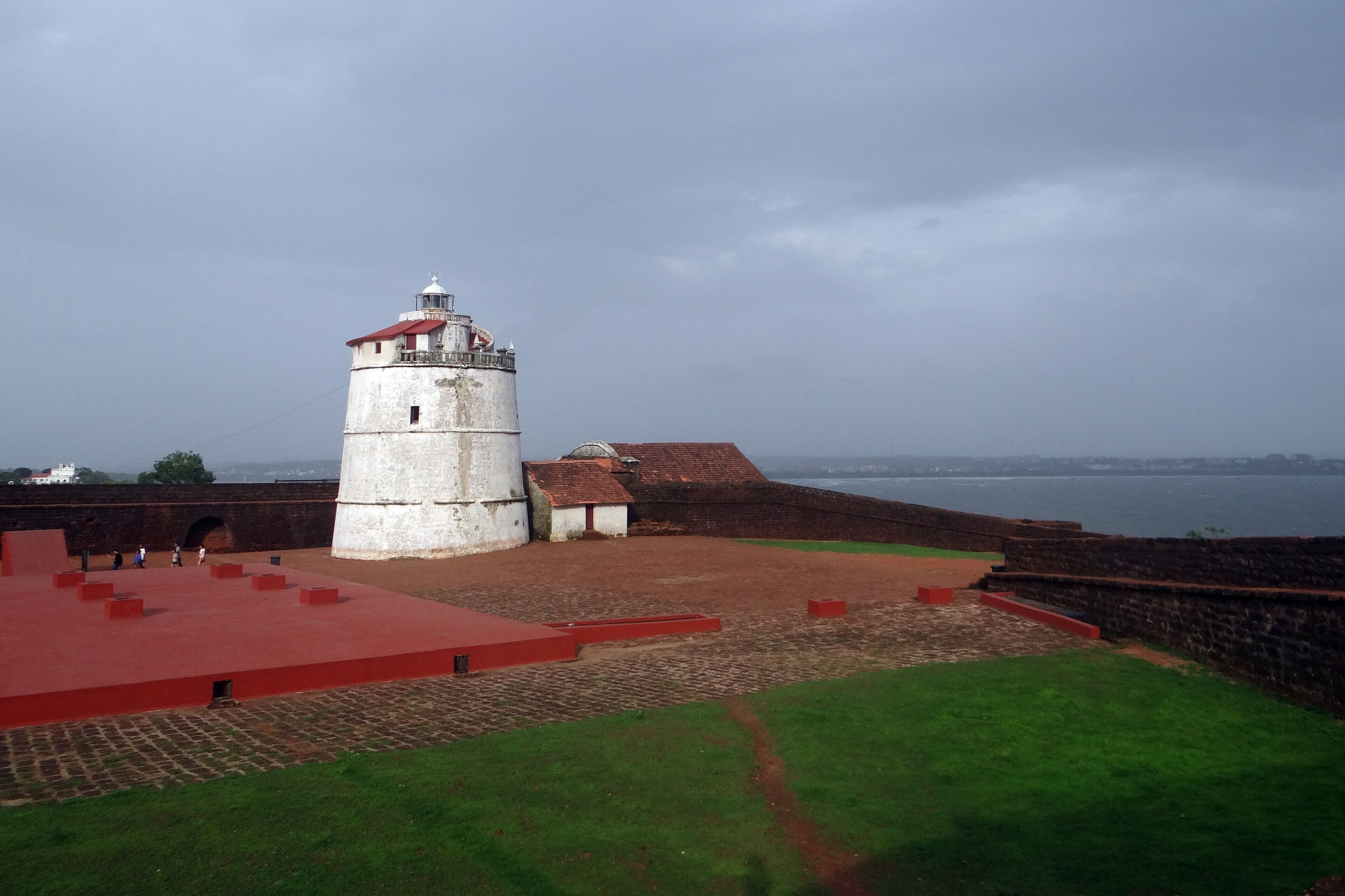 A historic fort with a prominent lighthouse, a paved courtyard, and a view of the sea.