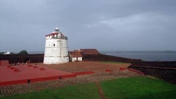 A historic fort with a prominent lighthouse, a paved courtyard, and a view of the sea.