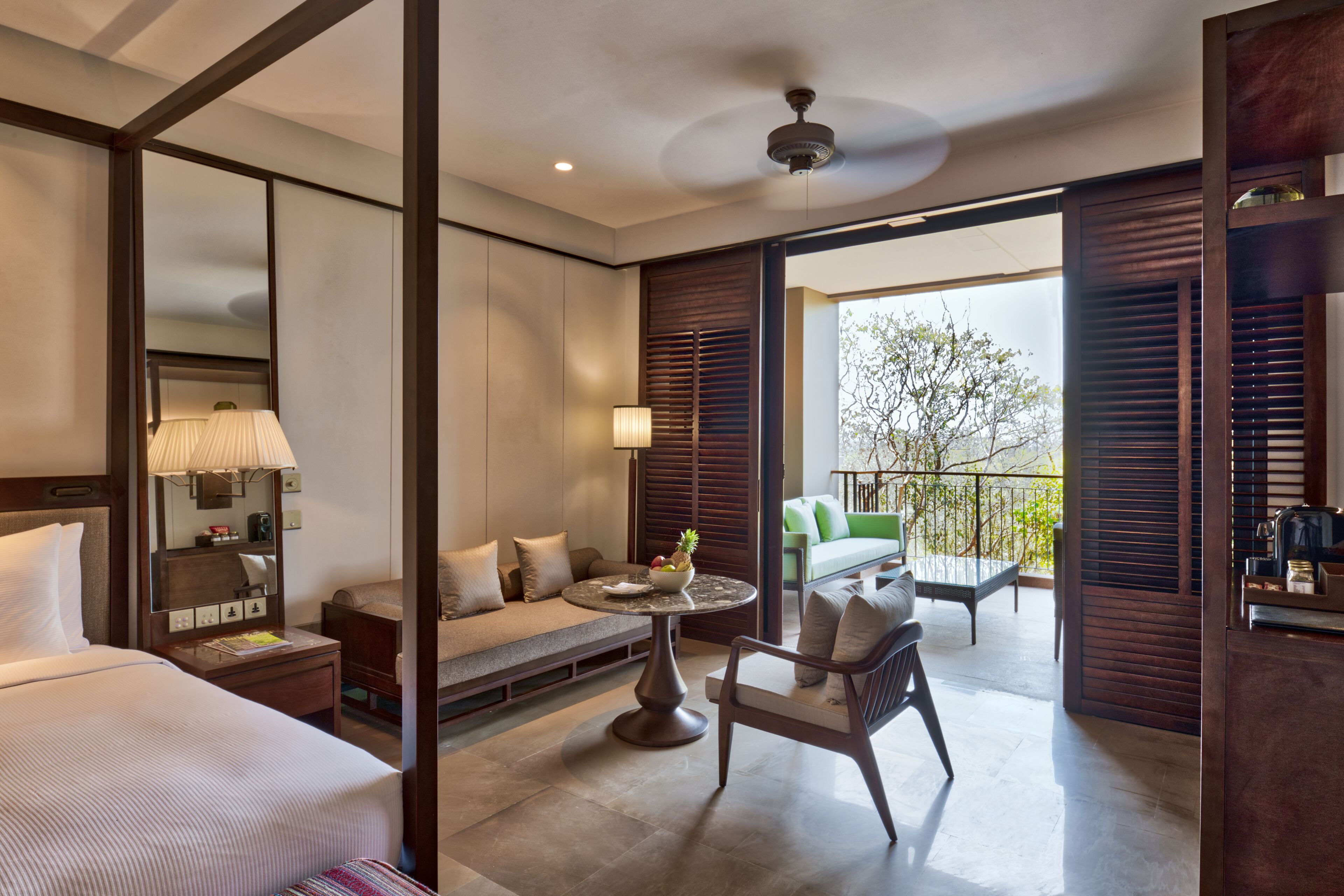 A hotel room with a bed, a sofa, a dining table, and a balcony with outdoor seating.