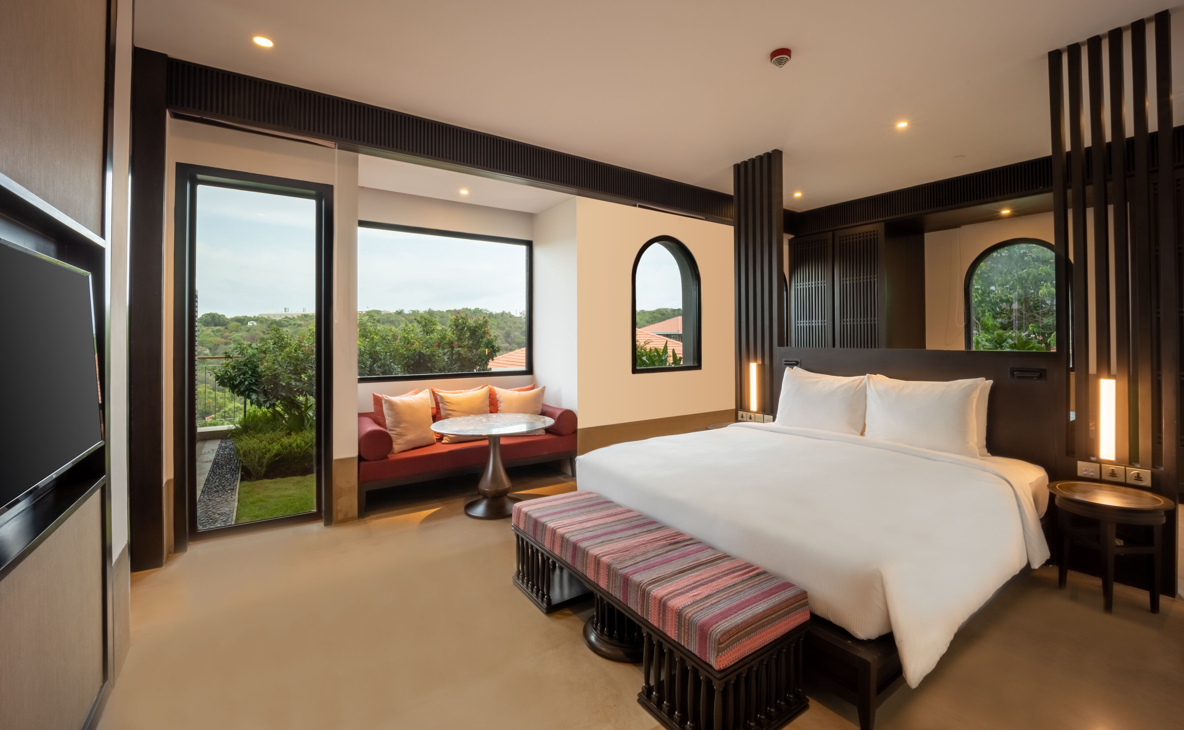 A modern hotel room with a large bed, a seating area with a view, and a balcony.