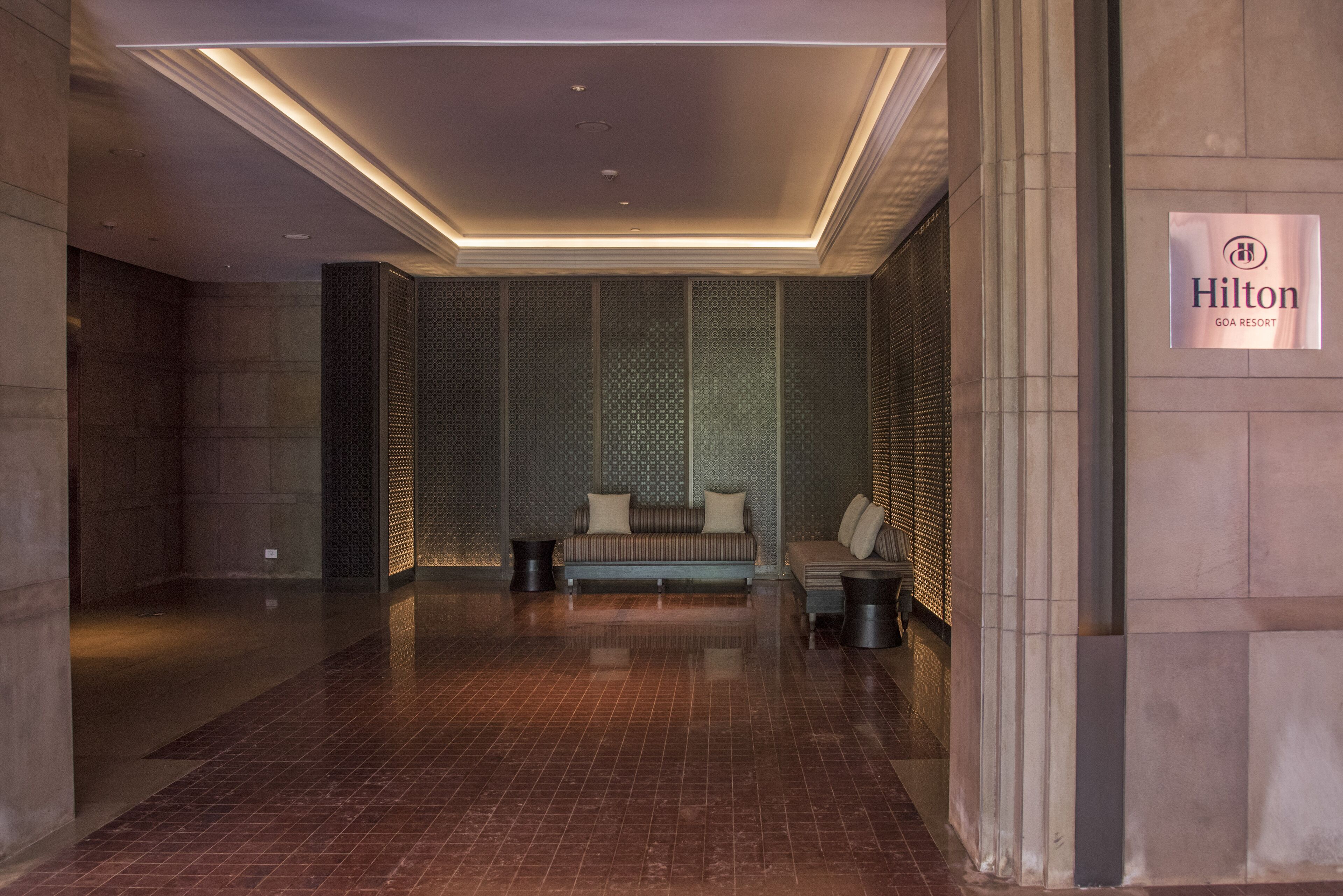 A modern lobby with a seating area, a sign for Hilton Goa Resort, and a patterned wall.