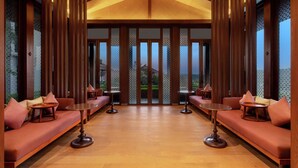 A modern hotel lobby with wooden paneling, cushioned seating, and round tables. - Hilton Goa Resort Candolim (Candolim)