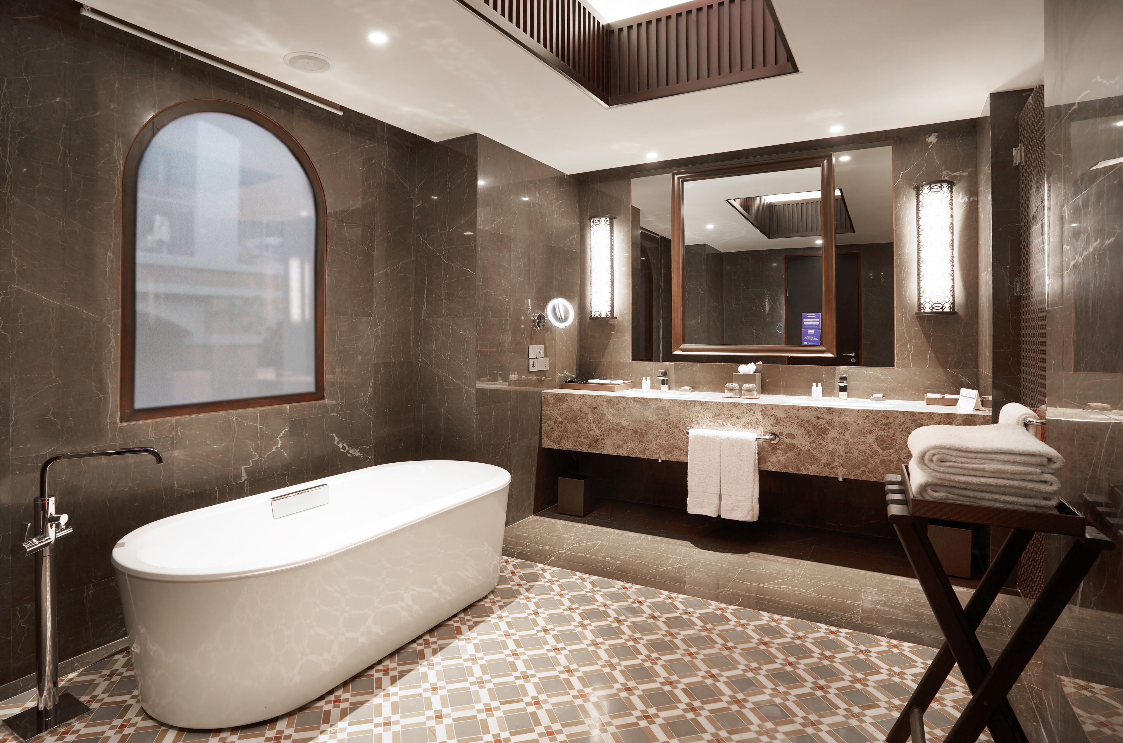 A modern bathroom with a freestanding bathtub, a large mirror, and a vanity with a towel rack.