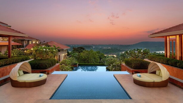 A poolside area with two lounge chairs and a view of the landscape. - Hilton Goa Resort Candolim (Candolim)