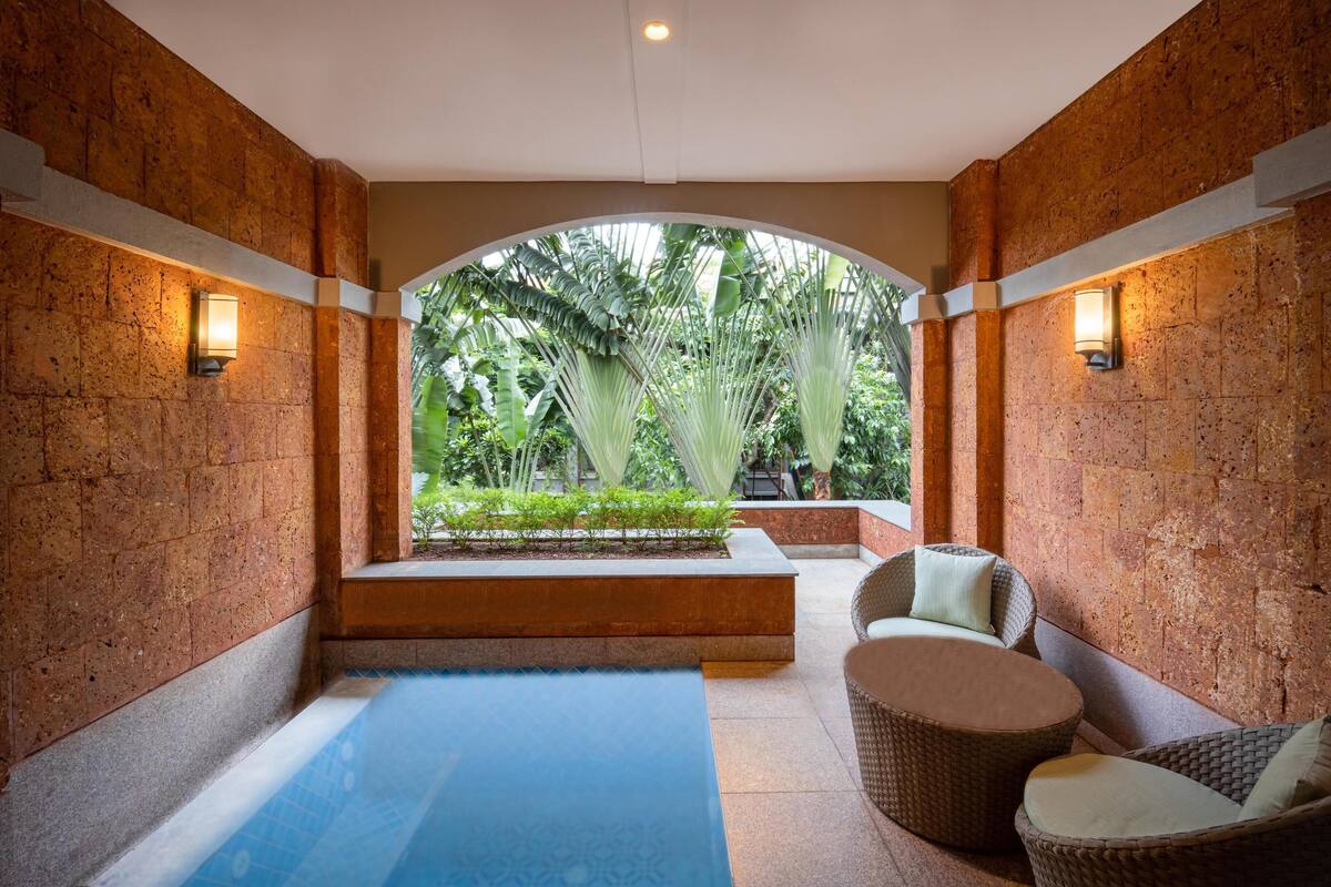 A spa area with a pool, wicker furniture, and a view of lush greenery.