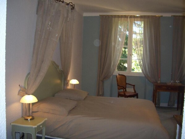 Un dormitorio con una cama, dos lámparas de noche, una silla y una ventana con cortinas.