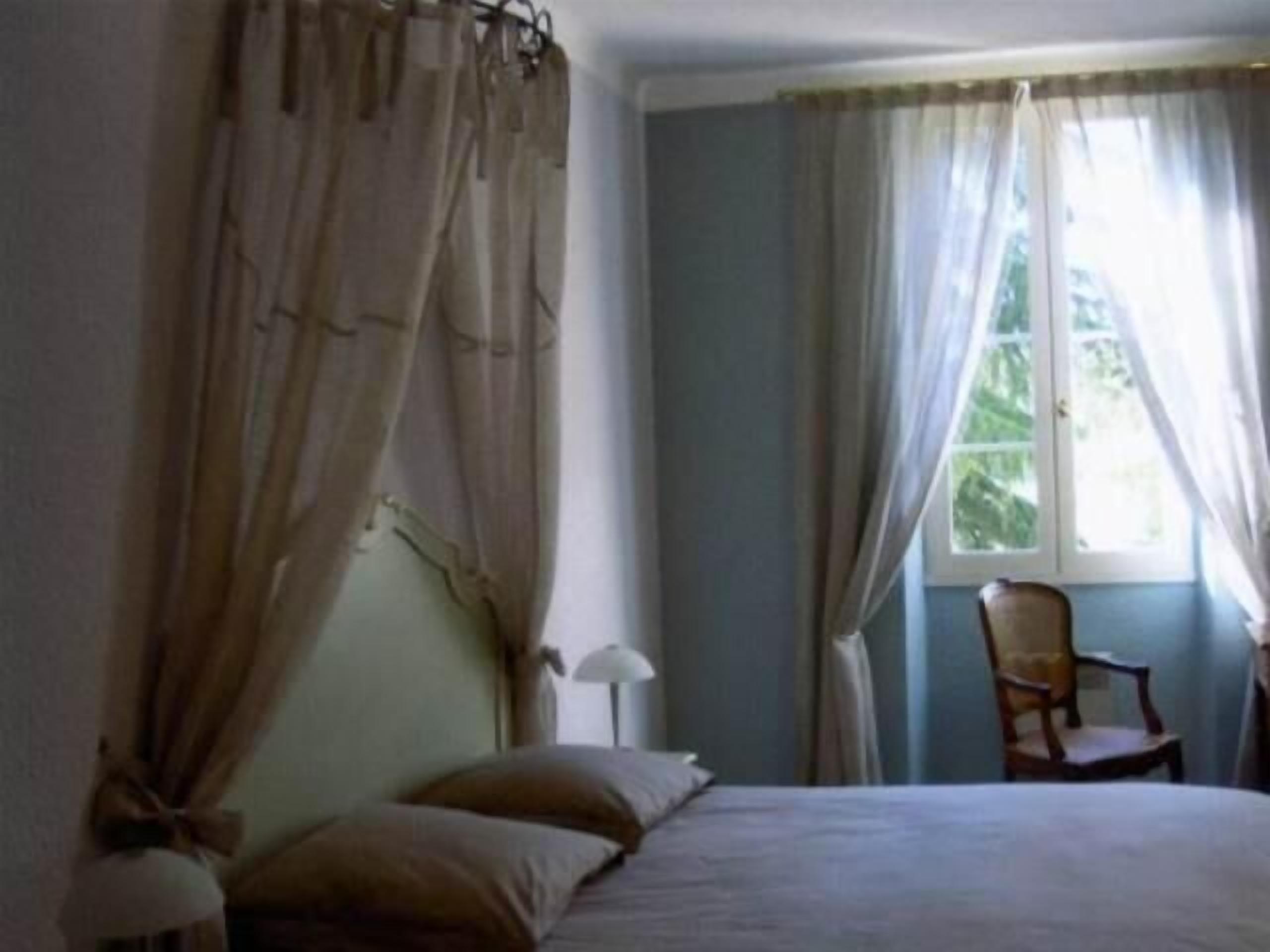 Un dormitorio con cama, una silla y ventana con cortinas.