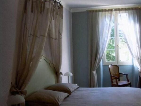 Un dormitorio con cama, una silla y ventana con cortinas.