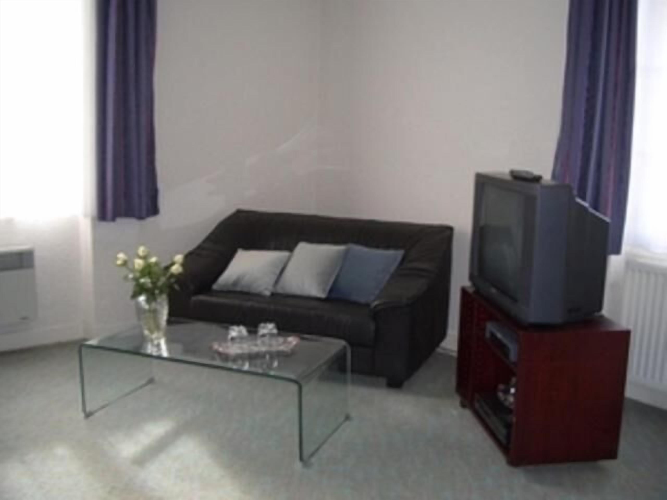 A living room with a dark sofa, a glass coffee table, a vase with flowers, and a television on a wooden stand.