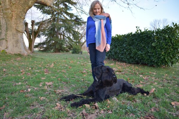 Una persona está de pie junto a un perro negro en un parque con césped y árboles.