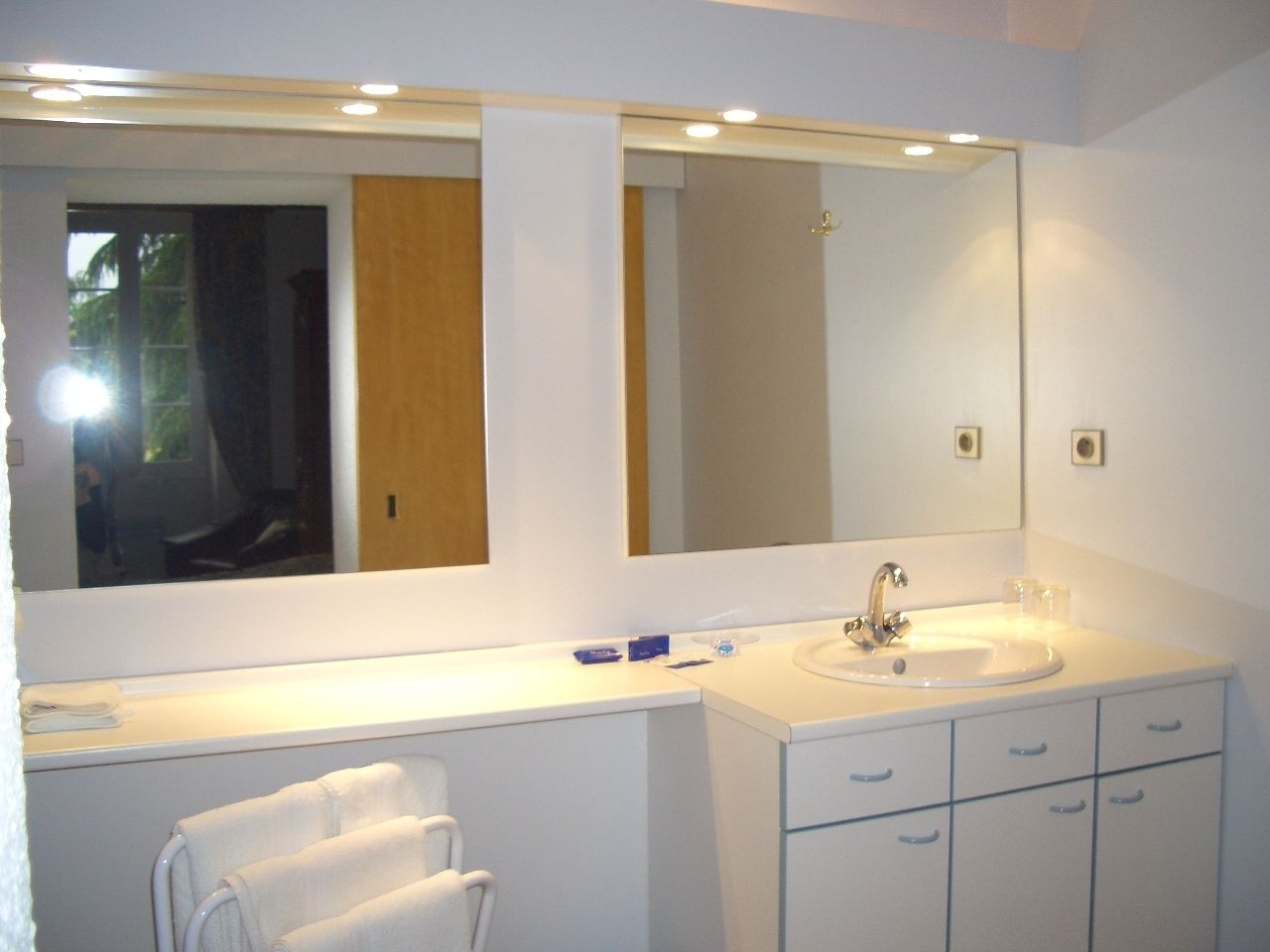 A modern bathroom with a large mirror, a sink, and a towel rack.