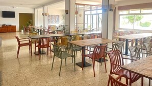 Una àmplia zona de dinar amb diverses taules i cadires, un televisor de pantalla plana penjat a la paret i grans finestres que proporcionen llum natural.