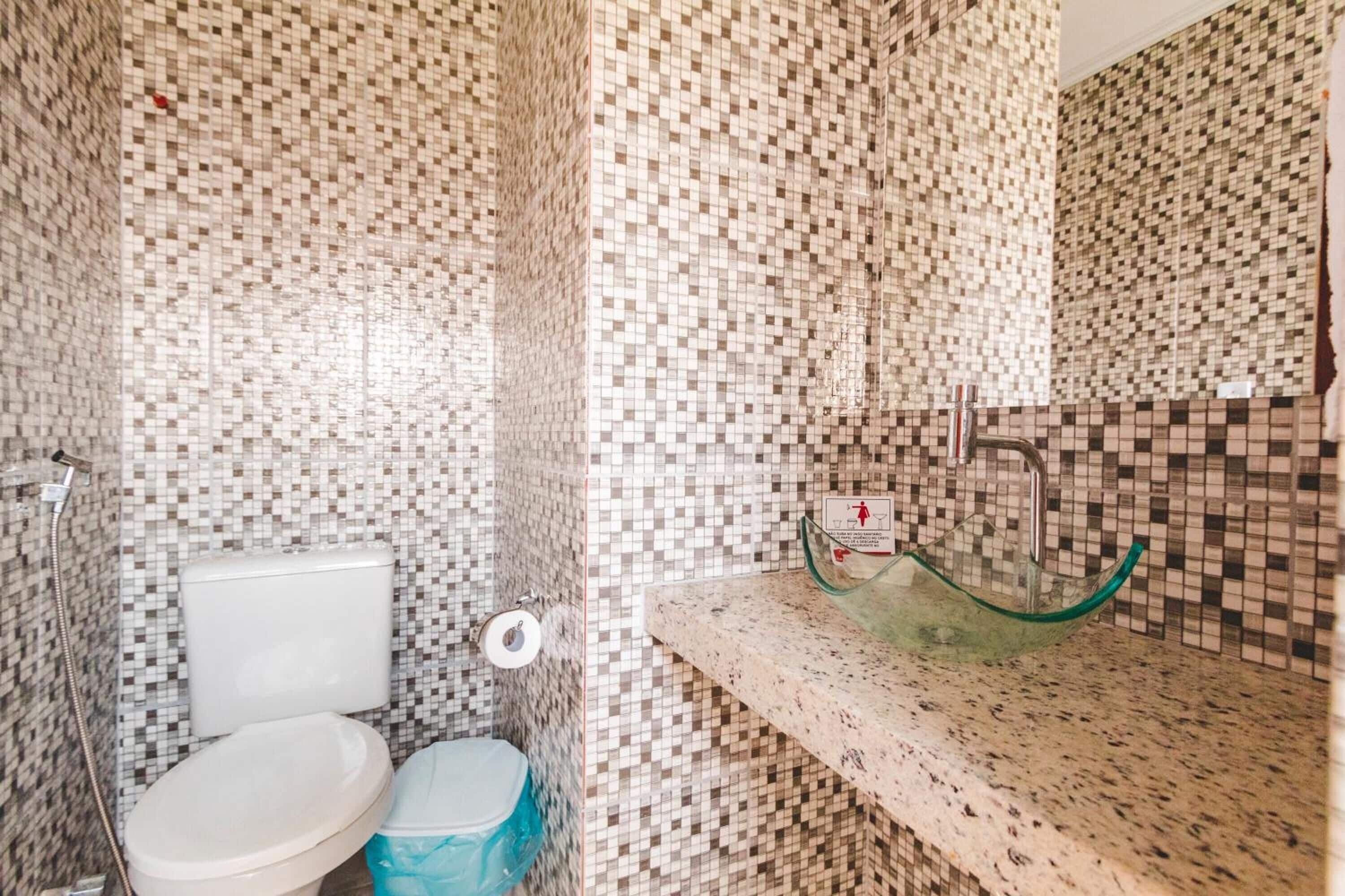 A bathroom with mosaic tile walls, a toilet, a bidet, and a glass sink.