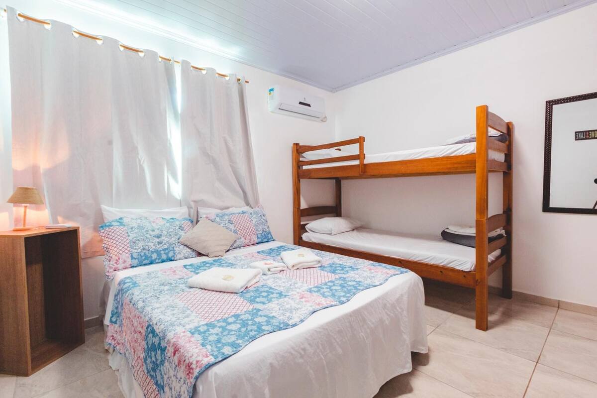 A bedroom with a bunk bed, a single bed, and a bedside table with a lamp.