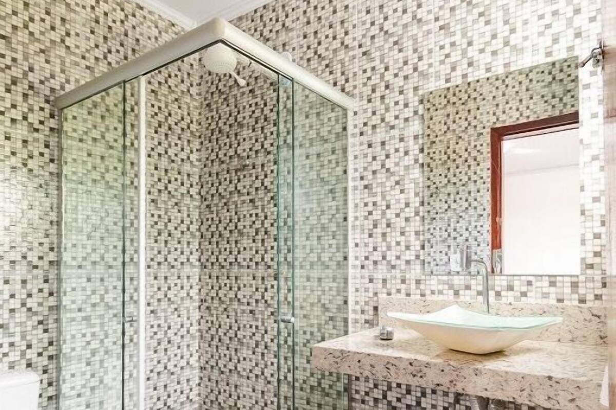 A bathroom with a glass-enclosed shower, a sink with a mirror, and a tiled floor.